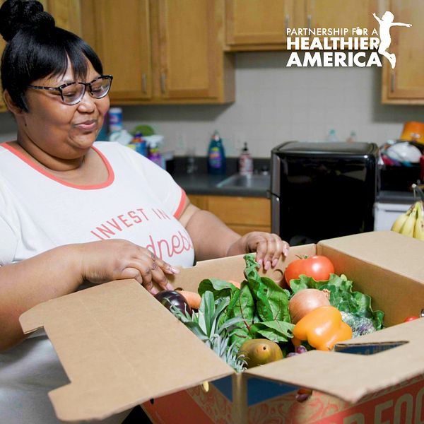 Charmaine from Good Food for All in New Orleans, LA looking at a produce box filled with fresh fruits and vegetables