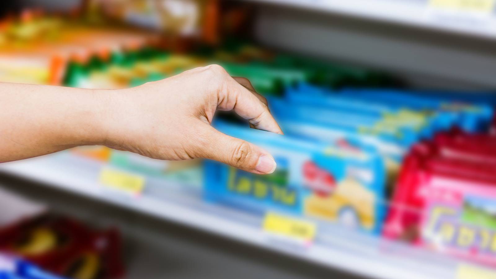 Image of a hand reaching for products on a convenience store shelf. 