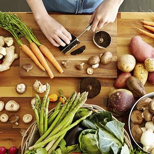 High angle point of view of female hands cutting Portobello mushrooms. Various fresh and healthy vegetables are on wooden table. Woman is cooking food. She is domestic kitchen.