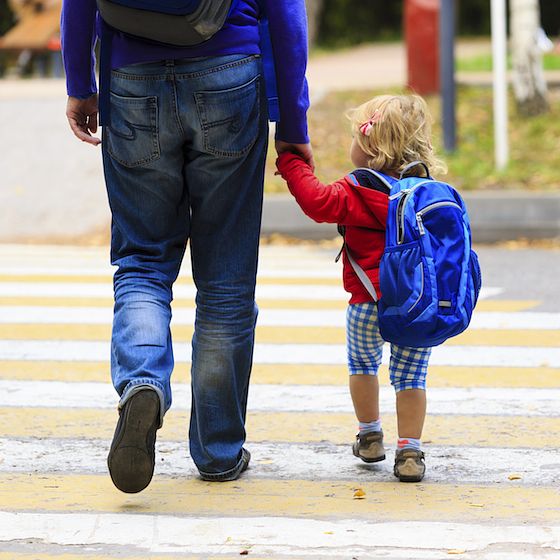 Image of child holding a parent's hand while walking to the first day of kindergarten. 