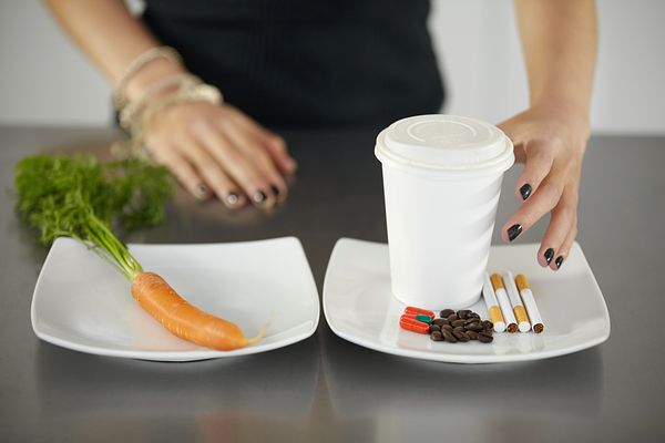 Image of a carrot on one plate and pills and cigarettes on another plate. 