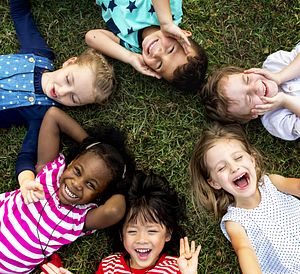 Group of diverse children laying in the grass looking up into the photographer's camera. 