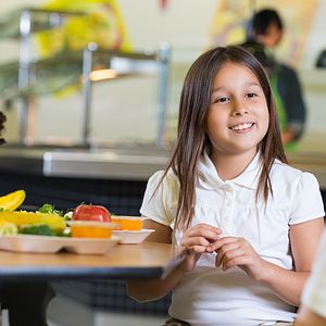Elementary school student in cafeteria holding a lunch tray with healthier food options.