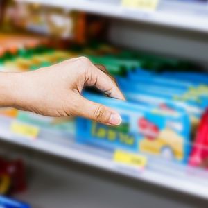 Image of a hand reaching for products on a convenience store shelf. 