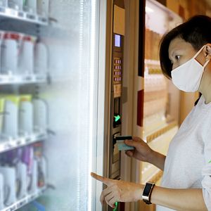 Women in mask looking at vending machine