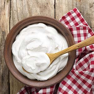 Image of plain yogurt in a bowl with a wooden spoon.