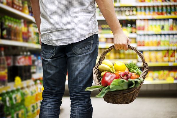 Person standing with a basket of veggies in a store