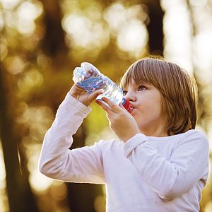 Image of young girl drinking water outdoors. 