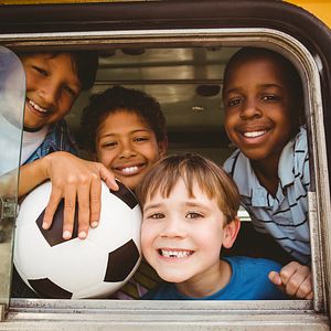 Image of elementary school boys with their heads poking out the window of a yellow school bus. 