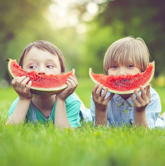 Image of two children eating watermelon slices outdoors. 