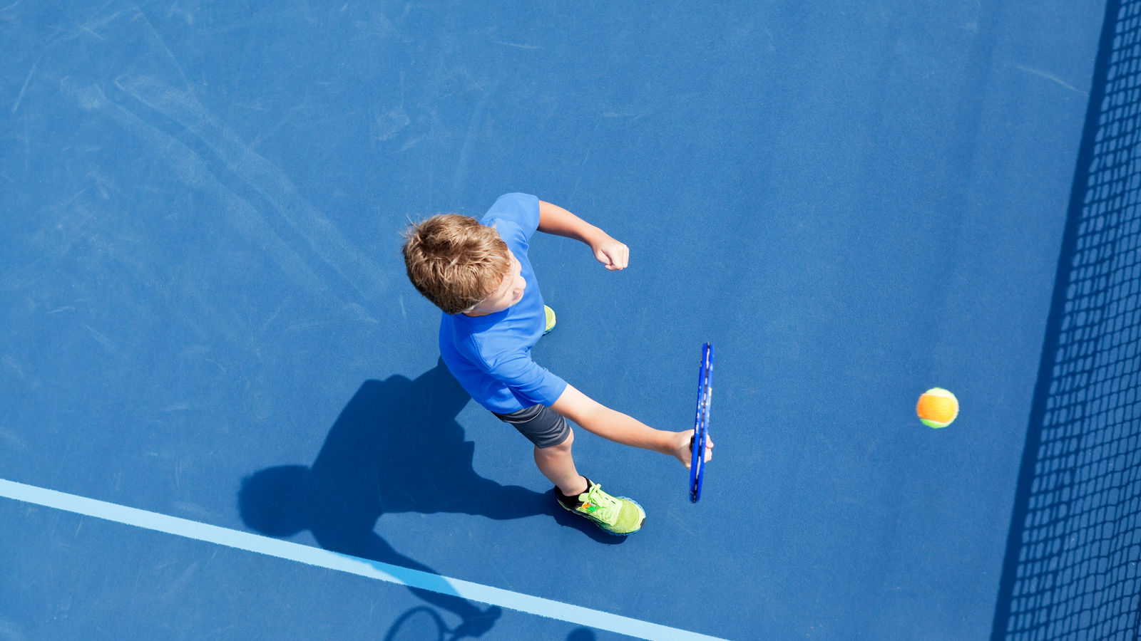 Boy playing tennis on a blue court.