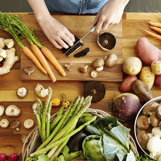 High angle point of view of female hands cutting Portobello mushrooms. Various fresh and healthy vegetables are on wooden table. Woman is cooking food. She is domestic kitchen.