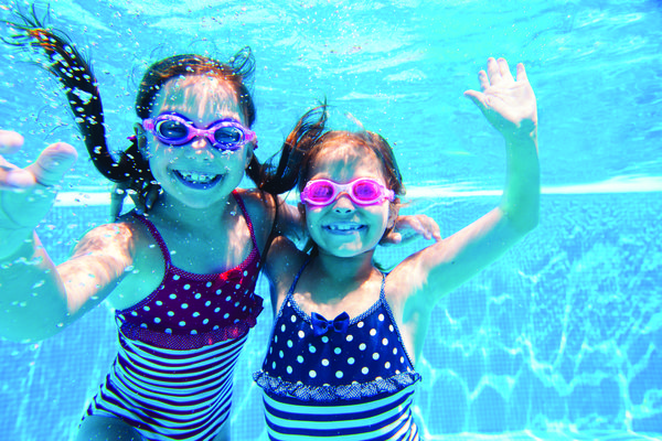 Image of two young girls swimming and posing in a pool.