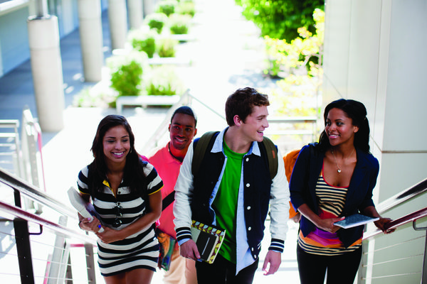 Image of a college student with a laptop on a campus lawn. 