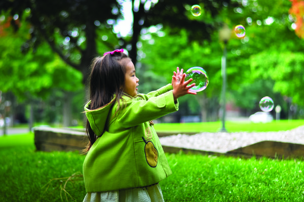 Image of a girl in a rain coat popping bubbles outdoors.