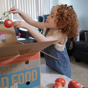 Ariel, a child in a Good Food for All participant family reaches into food box from PHA