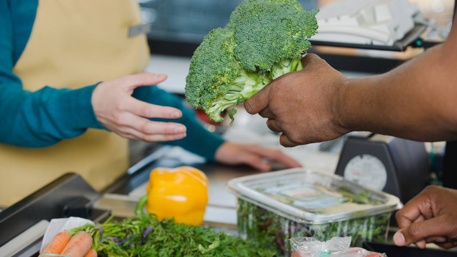 Customer handing produce over to cashier at grocery store register.