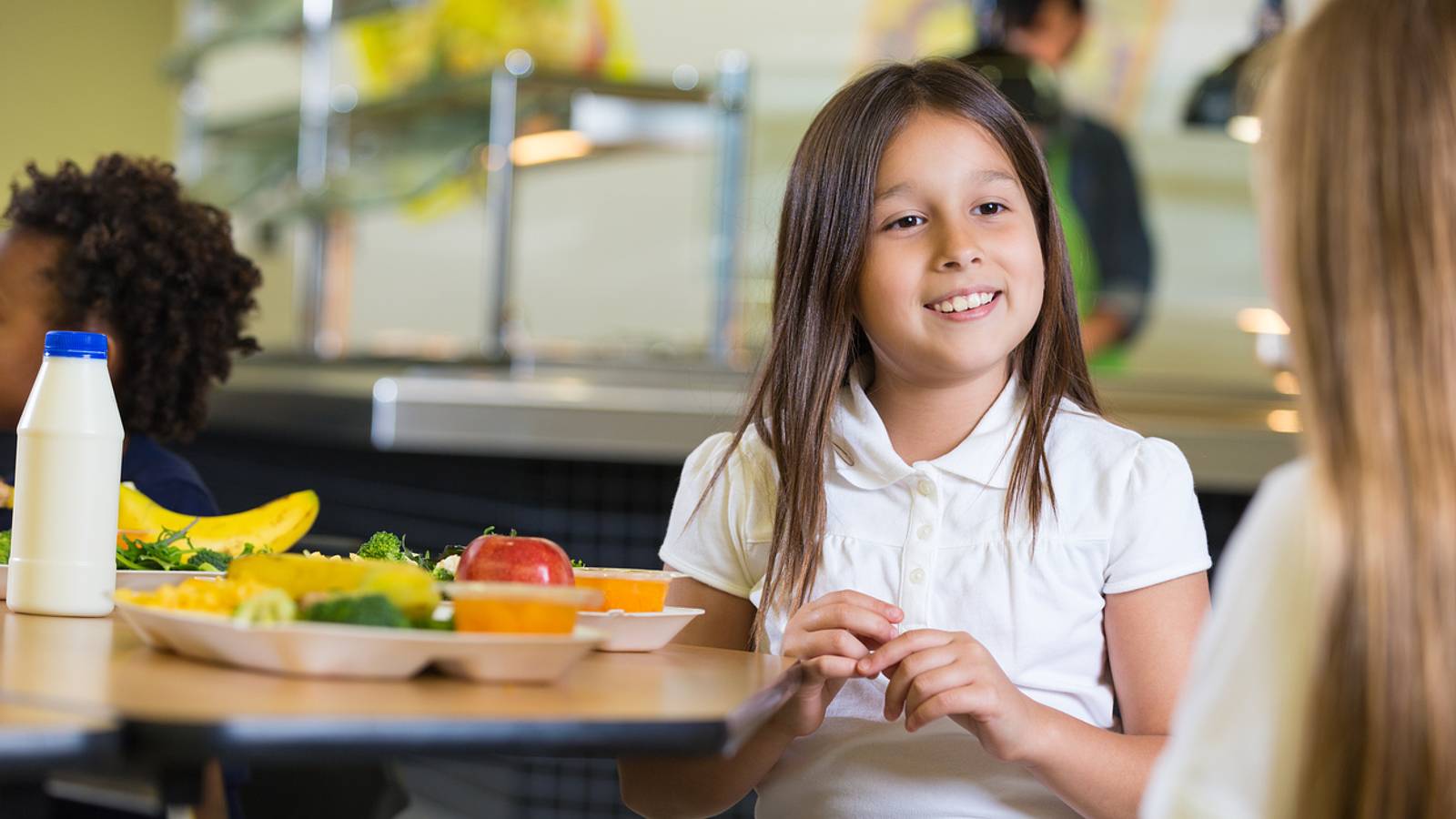 Elementary school student in cafeteria holding a lunch tray with healthier food options.