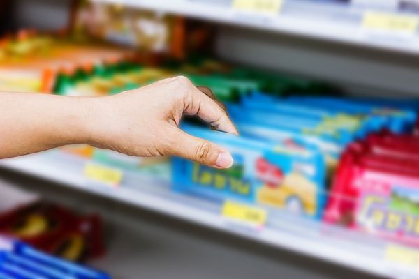 Image of a hand reaching for products on a convenience store shelf. 