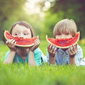 Image of two children eating watermelon slices outdoors. 